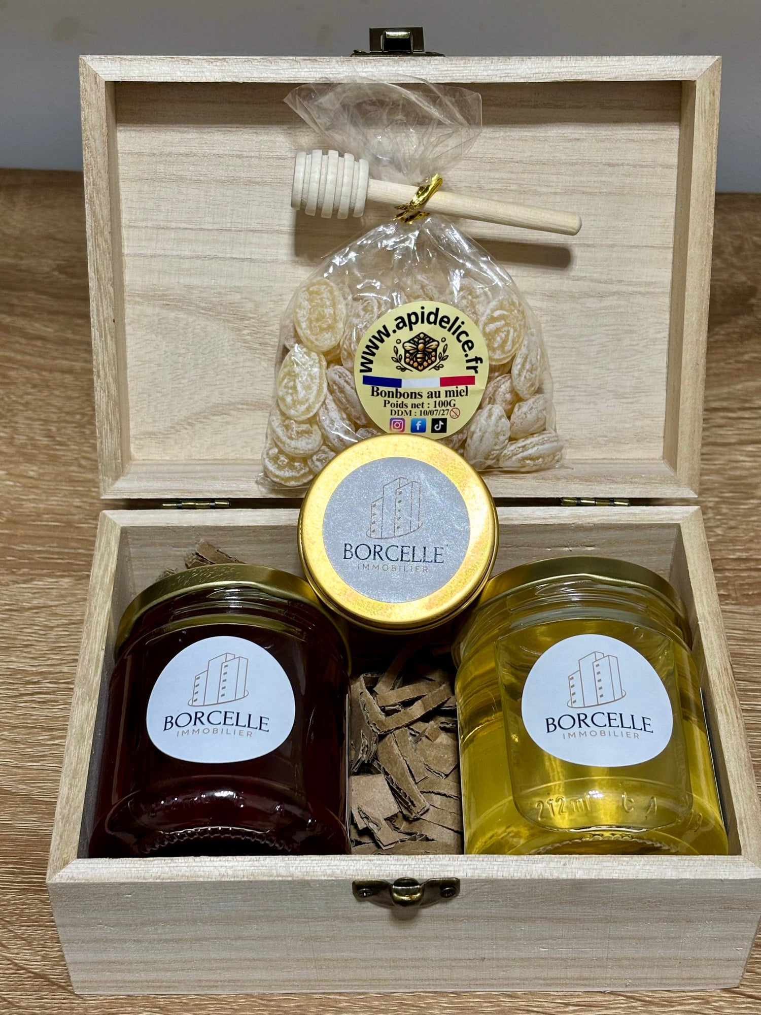 Coffret cadeau en bois d'entreprise personnalisé Borcelle Immobilier contenant deux pots de miel, une cuillère à miel et un sachet de bonbons au miel.