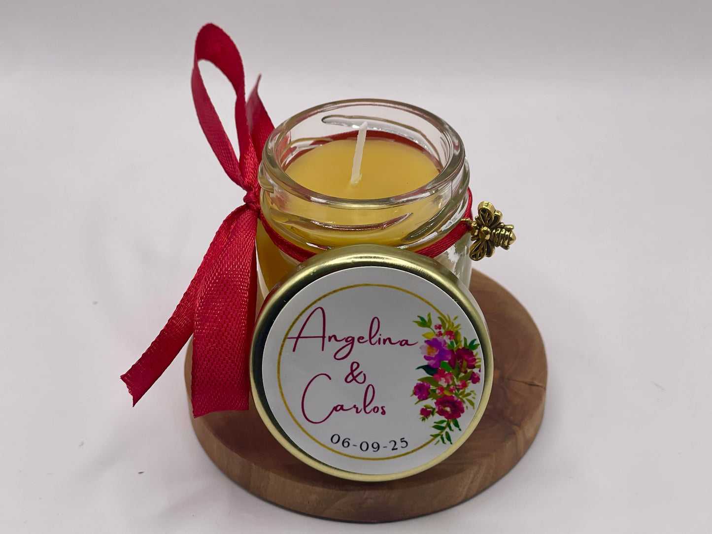 Illuminez votre grand jour avec un cadeau d'invité de mariage original, chaleureux et 100 % naturel. Découvrez notre mini bougie personnalisée, coulée à la main à base de cire d'abeille. Avec son sticker fleuri aux teintes fuchsia éclatantes (modèle Angelina & Carlos), son ruban de satin rouge et son délicat charm d'abeille dorée, c'est le souvenir de mariage parfait qui change des dragées traditionnelles. Une création artisanale et soignée à configurer sur apidelice.fr !