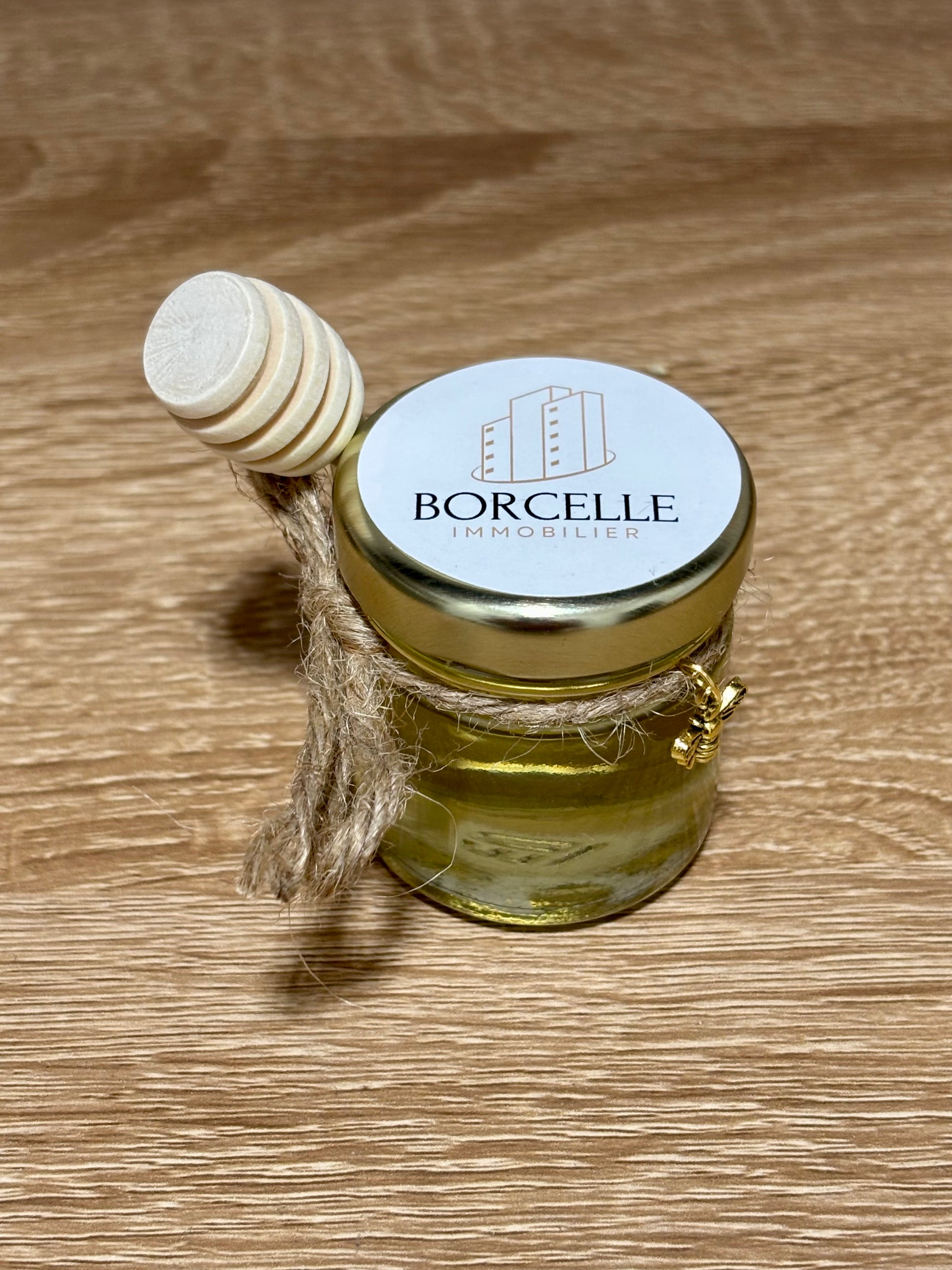 Mini pot en verre de miel d'acacia artisanal avec cuillère à miel en bois, nœud en ficelle de jute, charme abeille dorée et étiquette personnalisée Borcelle Immobilier.