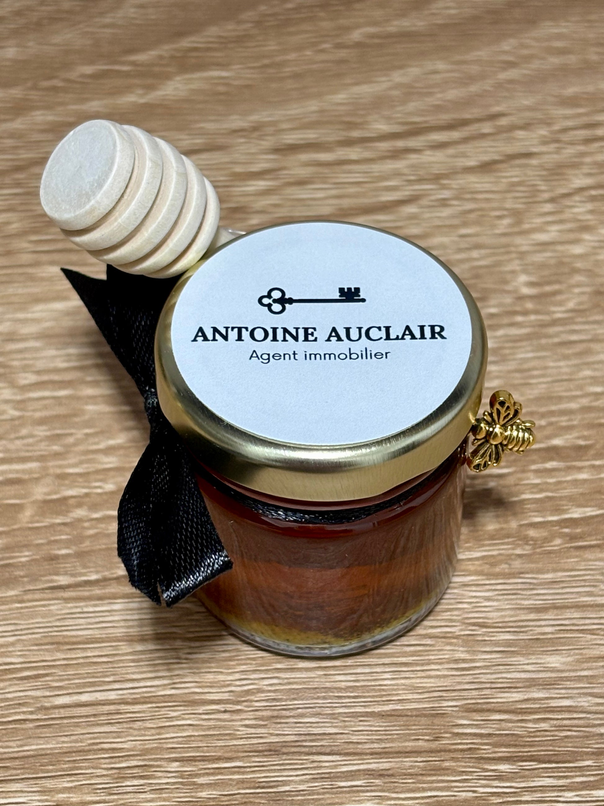 Mini pot en verre de miel de châtaignier artisanal avec petite cuillère en bois, ruban noir, charme abeille dorée et étiquette personnalisée Antoine Auclair.